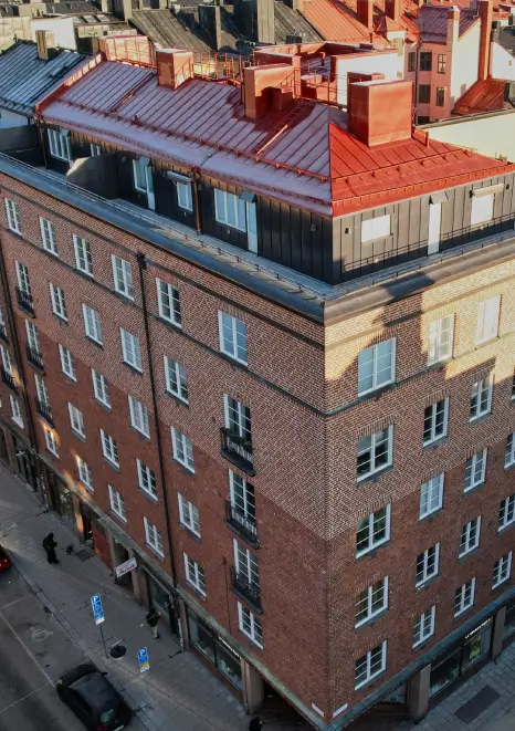 Tegelfasad med rött falsat plåttak på flerbostadshus, ett typiskt projektområde för Kinnunens Plåtslageri AB inom tak- och plåtarbeten
